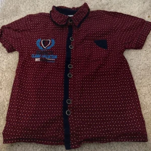 Röd kortärmad skjorta med mönster - Snygg röd skjorta med små vita prickar och blå detaljer. Skjortan har korta ärmar och en bröstficka. Den är dekorerad med broderi på framsidan och har knappar längs hela framsidan.