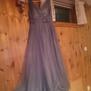 Lila långklänning  - Elegant grå långklänning med v-ringad urringning och blommiga detaljer i midjan. Klänningen har använts precis en gång. Köpt för nästan 2000kr