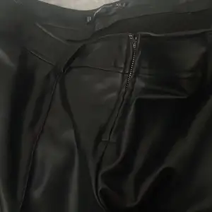 Snygga svarta skinnbyxor med dragkedja framtill. Perfekta för en trendig look och kan stylas på många sätt. Byxorna har en högmidjad passform som ger en smickrande siluett.