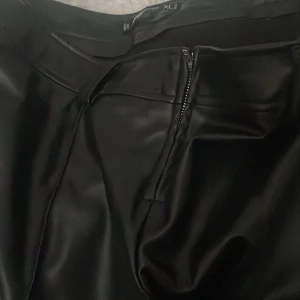 Svarta skinnbyxor med dragkedja - Snygga svarta skinnbyxor med dragkedja framtill. Perfekta för en trendig look och kan stylas på många sätt. Byxorna har en högmidjad passform som ger en smickrande siluett.