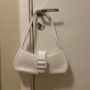 Vit axelväska med spänne - Liten vit väska med spänne framtill, väskan är aldrig använd därav nyskick.