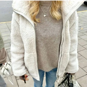 Vit teddyjacka med dragkedja - Mysig vit teddyjacka med dragkedja och hög krage. Perfekt för kyliga dagar med sin fluffiga och varma design. Jackan har långa ärmar och två praktiska fickor framtill. Det är en. XL men är som en S,M