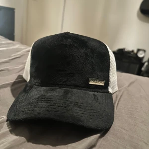 Svart och vit keps från Maggiore - Snygg keps från Maggiore med svart framsida och vit mesh-baksida. Perfekt för en avslappnad stil. Justerbar passform med tryckknappar.