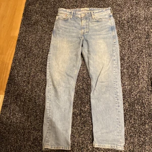 Blå jeans från Jack & Jones - Säljer ett par ljusblå jeans från Jack & Jones i modellen Loose/Chris. De har en klassisk femficksdesign och knappgylf. Perfekta för en avslappnad stil.