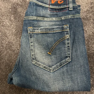 Blå jeans från dondup - Snygga blå jeans med klassisk femficksdesign och kontrastsömmar. De har en normal passform och är perfekta för en avslappnad stil. Jeansens slitna look ger dem en trendig touch. Modell George storlek 34. Skulle inte säga att snus effekten på vänster bakficka är en defekt utan rätt så stiligt🤝