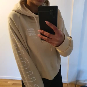 Beige hoodie med tryck - Säljer en beige hoodie med tryck på ärmen och bröstet. Den har en justerbar huva med dragsko och ribbade muddar vid ärmslut och nederkant. Perfekt för en avslappnad stil i stl S oversized