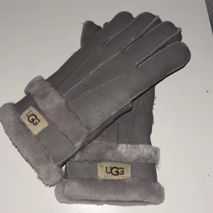 Grå skinnhandskar från UGG - Snygga och varma grå skinnhandskar från UGG med mjukt foder och uppvikta muddar. Perfekta för kalla dagar med stilren design och UGG-logga på mudden. Använda 10 gånger
