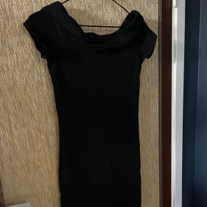 Svart klänning med offshoulder-design - Säljer en elegant svart klänning med en stilren offshoulder-design. Klänningen är figurnära och perfekt för festliga tillfällen. Materialet känns mjukt och bekvämt mot huden. Passar utmärkt för en kväll ute eller en speciell tillställning. 🖤