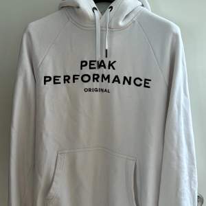 Säljer en snygg och bekväm vit hoodie från Peak Performance. Den har en klassisk design med svart text på bröstet och en praktisk magficka. Lite slitage vid armmuddarna annars i bra skick (ses sista bild). Köpt för ungefär 1200 kronor.