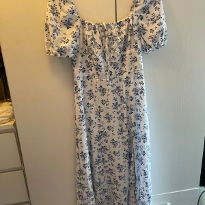 Klänning  - Klänning med blommigt mönster i mycket gott skick. Har en slits vid ena sidan 