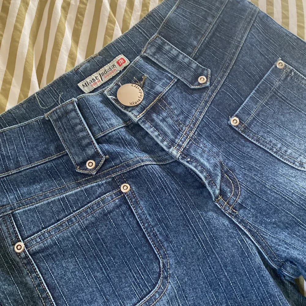 Säljer ett par snygga blå jeans med  bootcut och låg midja. De har coola detaljer som stora fickor bak och en knapp med logga framtill. Perfekta för en retro look! Fint skick!. Jeans & Byxor.