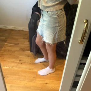 Ljusblå jeanskjol - Säljer en superfin ljusblå jeanskjol med rå kant och slitna detaljer. Perfekt för sommardagar eller en avslappnad vårlook. Kjolen har en klassisk femficksdesign och stängs med knapp och dragkedja framtill. Den är i en normal passform och ger en cool och avslappnad stil.