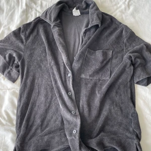 Grå frottéskjorta från H&M - Säljer en grå frottéskjorta/overshirt från H&M i storlek M. Skjortan har korta ärmar och knappar framtill. Den är mjuk och bekväm, perfekt för en avslappnad stil. Frågor? Skriv!