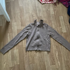 Beige kofta från Noisy May - Säljer en snygg brun kofta från Noisy May. Den är i storlek S och har en dragkedja framtill. Perfekt för höst och vinter, den är både stilren och bekväm. Koftan har långa ärmar och är gjord av ett mjukt material som håller dig varm. Passar bra till både vardag och fest!