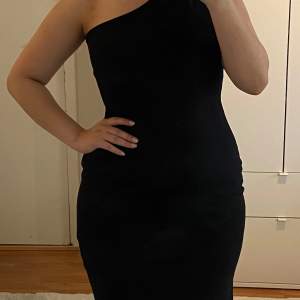 Snygg och elegant svart oneshoulder klänning som passar perfekt för festliga tillfällen. Klänningen har en tight passform som framhäver figuren och ger en stilren look. Materialet är mjukt och bekvämt, vilket gör den skön att bära hela kvällen. Använd en gång, därav mycket bra skick! Jag är 160 cm och den slutar ovanför mina knän. Storlek L.