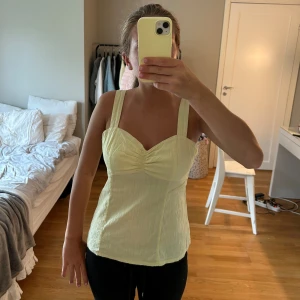 Gul topp från Orsay - Säljer en söt gul topp från Orsay. Den har breda axelband och en snygg rynkad detalj framtill. Perfekt för sommardagar och kan enkelt matchas med jeans eller kjol. Toppen är i ett lätt och bekvämt material.
