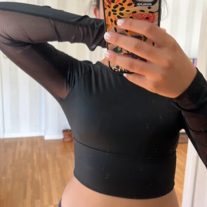 Svart långärmad topp med öppen rygg - Säljer en svart tränings långärmad topp i storlek S. Toppen har en tight passform och är tillverkad i ett syntetmaterial. Den har en öppen rygg och meshdetaljer på ärmarna. 