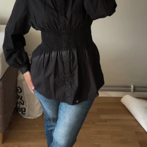 Skjorta med smockad midja - Svart skjorta med smockad midja från H&M. Använd endast ett par gånger, som ny.  Storlek S men funkar för M.