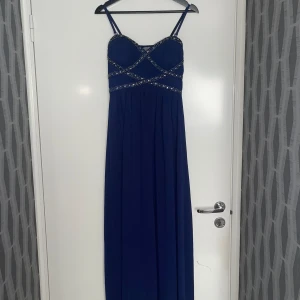 Lång marinblå balklänning  - Lång marinblå bal/fest klänning som går att använda med eller utan axelbanden. Klänningen är använda vid 2 tillfällen (bal och bröllop). Alla pärlor och paljetter sitter kvar och inget fattas. Klänningen är i nyskick utan fel. Nypris var 999:-