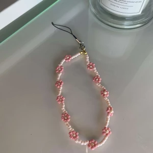 Mobilaccesoar  - Egengjord mobilaccesoar med pärlor av olika rosa som utgör en blommdesign. 