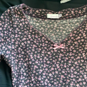Blommig tröja från Blanco - Säljer en superfin blommig tröja från Blanco. Den är väldigt varm och är i bra kvalitet med ett sött rosa blommönster på en grå bakgrund. Tröjan har en v-ringning med en liten rosett som detalj och trekvartsärmar. Perfekt för både vår och höst!