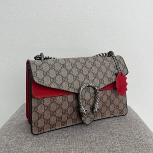 Gucci axelväska med monogram - Säljer en superfin Gucci axelväska med det klassiska GG-monogrammet. Väskan har en snygg kombination av beige och rött, med en cool kedjerem och ett unikt spänne framtill. Insidan är klädd i röd mocka och har en praktisk dragkedja. Kontakta innan köp