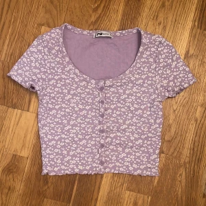 Lila t-shirt med vita blommor - Bara använd ett fåtal gånger. Är i nytt skick 