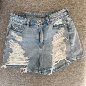 Säljer ett par ljusa jeansshorts från American Eagle. De har en cool, sliten look med stora revor på framsidan. Perfekta för en avslappnad sommarstil! 🕶️