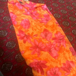 Orange och rosa blommig klänning från Shein - Säljer en färgglad och somrig klänning från Shein i storlek S. Klänningen har ett vackert blommigt mönster i orange och rosa toner. Perfekt för sommarens fester eller en dag på stranden!