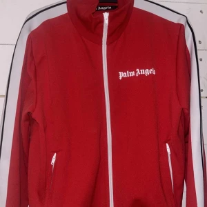 Röd track jacket från Palm Angels - Säljer min track suit tröja från Palm angels pga att jag ej använder den, bra skick o finns inga tecken på användning. Den hänger bara här hemma och används aldrig! Hör av er vid intresse!