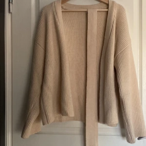 Beige ribbad kofta med knytband - Säljer en mysig beige kofta med ribbad struktur och knytband framtill. Perfekt för kyliga dagar och enkel att matcha med olika outfits. Koftan har långa ärmar och en avslappnad passform. Köpt från Shein 