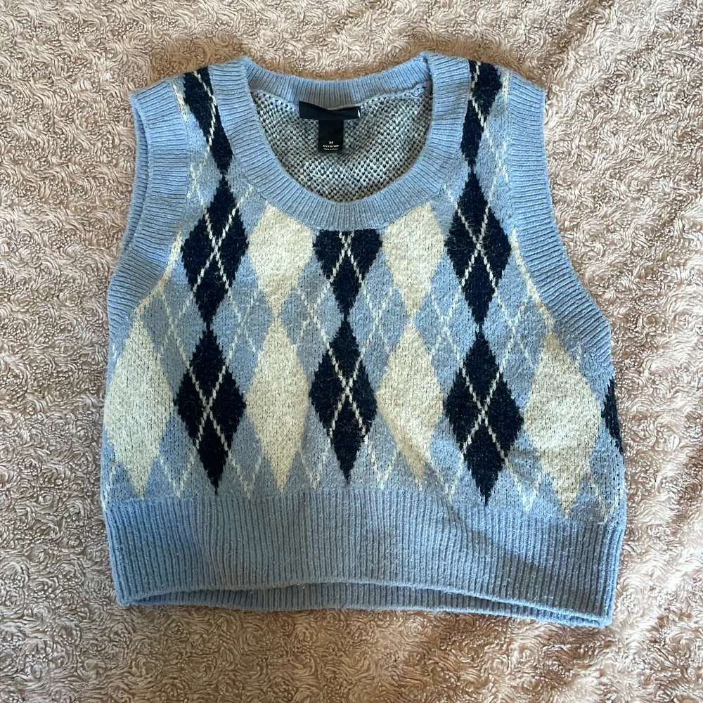 Säljer en snygg ljusblå stickad väst från Monki med ett klassiskt argylemönster i mörkblått och vitt. Perfekt för lager-på-lager-stil och ger en retro touch till din outfit. 🧶✨. Yläosat.