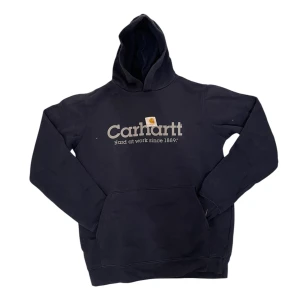 Marinblå Carhartt hoodie - Säljer en marinblå hoodie från Carhartt med tryck på framsidan. Den har en klassisk känguruficka och en bekväm huva. Perfekt för en avslappnad stil. Igenkligen storlek XL men passar som S.