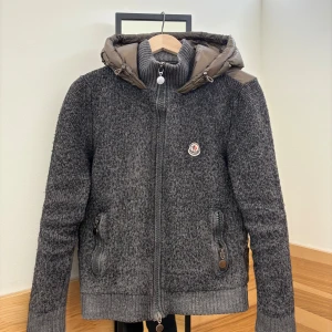 Moncler jacka - Snygg grå stickad jacka från Moncler med dunfylld huva och rygg. Jackan är extremt sällsynt och sälj knappt. Den är självklart äkta, den är i storlek L men har haft den i torktumlare för att minska den lite men blev för mkt så den sitter mer som XS. Tveka inte på att höra av er