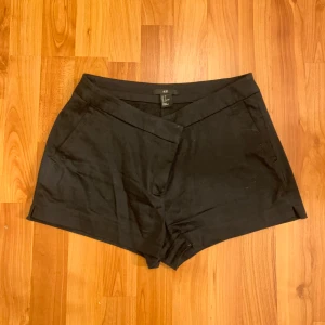 Svarta shorts från H&M - Snygga svarta shorts från H&M med en stilren design. De har en högmidjad passform och är perfekta för en chic look. Tillverkade i ett bekvämt material som liknar kostymbyxor.
