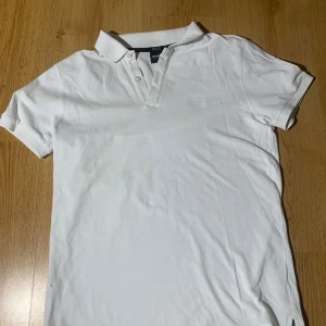 Vit pikétröja från Hugo Boss - Säljer en stilren vit pikétröja från Hugo Boss i. Tröjan har korta ärmar och en klassisk krage med knappar. Perfekt för en avslappnad men ändå elegant look.    Storlek S