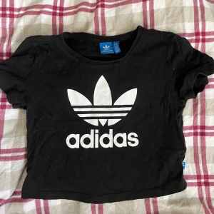 Svart croppad t-shirt från Adidas - Säljer en svart croppad t-shirt från Adidas. Använd några gånger när jag va yngre. Storlek 