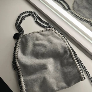 Stella McCartney liknande väska - Snygg grå väska med kedjedetaljer och magnetknäppning. Väskan har en unik design med synliga sömmar och ett leopardmönstrat foder. Perfekt för att ge din outfit en cool touch.