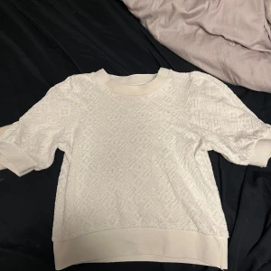 Vit kortärmad tröja från Holly & Whyte - Säljer en stilren vit tröja från Holly & Whyte by Lindex. Tröjan har korta ärmar och ett diskret mönster som ger en elegant touch. Perfekt för en avslappnad men ändå chic look. 