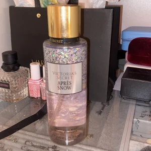 Victoria's Secret Après Snow Fragrance Mist - En glittrande doftmist från Victoria's Secret med namnet Après Snow. Flaskan har en skimrande design med guldlock och innehåller noter av holly berries och winter jasmine. Perfekt för att fånga vinterns magi. Nästan helt full 