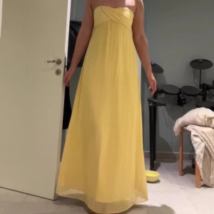 Gul axelbandslös balklänning  - Säljer en vacker gul axelbandslös långklänning med en elegant drapering över bysten. Perfekt för sommarens festligheter eller en speciell kväll. Klänningen har en mjuk och flödande passform som ger en romantisk känsla. 🌼Jag är 172cm lång och precis lagom lång för mig. Skicka för fler bilder!