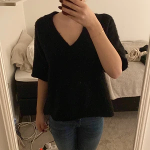 Svart stickad tröja från Sister Knitwear - Säljer en stilren svart stickad tröja från Sister Knitwear. Tröjan har en v-ringad design och korta ärmar, perfekt för en avslappnad look. Passar bra till jeans eller kjol. Perfekt för höst och vår!
