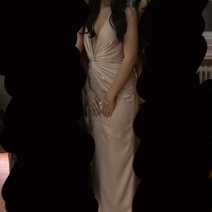 Champagnefärgad balklänning med knyt - Champagnefärgad balklänning i satin med  v-ringning och knyt i nacken. Använd endast en gång så fint skick. Köpt från PLT. Storlek 4 UK, vilket motsvarar XS eller S enligt mig. Dragkedja i sidan. Skriv för frågor☺️Pris kan diskuteras!