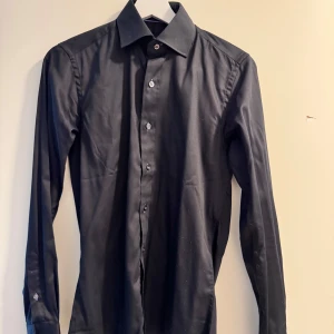 Mörkblå skjorta med knappar - Snygg mörkblå skjorta med klassisk krage och knappar hela vägen ner. Perfekt för en stilren look. Långärmad design som passar bra till olika tillfällen. Endast använd en gång.