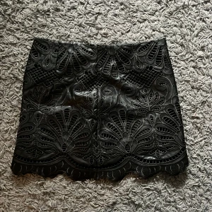 Svart kjol med spetsdetaljer - Snygg svart kjol från H&M med vackra spetsdetaljer och ett elegant mönster. Kjolen har en dragkedja i sidan för enkel på- och avtagning. Perfekt för att ge en stilfull touch till din outfit.