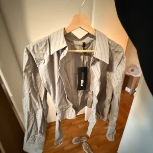 Grå randig skjorta  -  tunna ränder och långa ärmar. Skjortan har en klassisk krage och knappar framtill. Perfekt för en stilren look. Aldrig testat eller haft på mig den, glömde lämna tillbaka den så har den i gaderoben