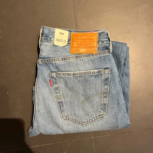 Helt nya Levis 501 jeans i blå denim - Klassiska Levis 501 jeans i blå denim med en straight passform. De har slitna detaljer på framsidan för en trendig look. Perfekta för en avslappnad stil. Nypriss 1349 mitt endast 500. 