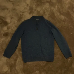 Blå cashmere tröja från Alaine Paine  - Säljer en stilren blå stickad tröja från Alaine Paine . Tröjan har en dragkedja vid halsen och långa ärmar. Perfekt för kyligare dagar.