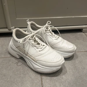 Vita sneakers med snörning - Snygga vita sneakers med snörning och perforerade detaljer. Skorna har en chunky sula och är tillverkade i syntetmaterial. Perfekta för en stilren look.