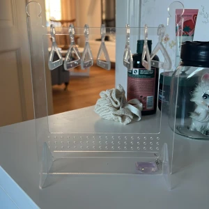 Genomskinlig smyckeshållare med krokar - Praktisk och stilren genomskinlig smyckeshållare med flera krokar för att organisera dina smycken. Perfekt för att hålla ordning på örhängen och halsband. Tillverkad i akrylmaterial för en modern och minimalistisk look.